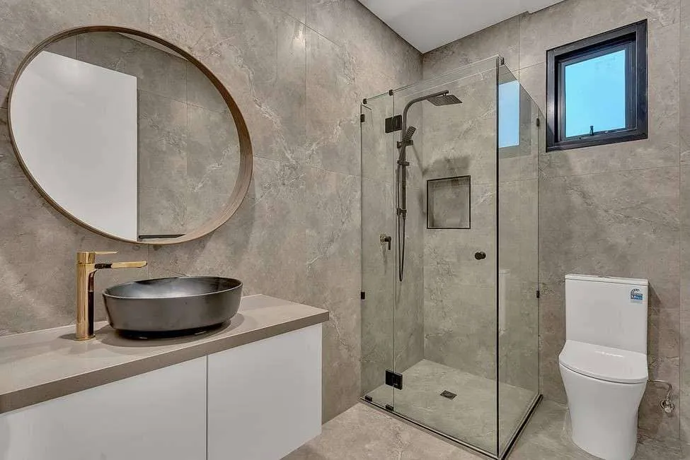 B-Spoke bathroom with grey tiles, a round mirror, dark vessel basin and brass tap