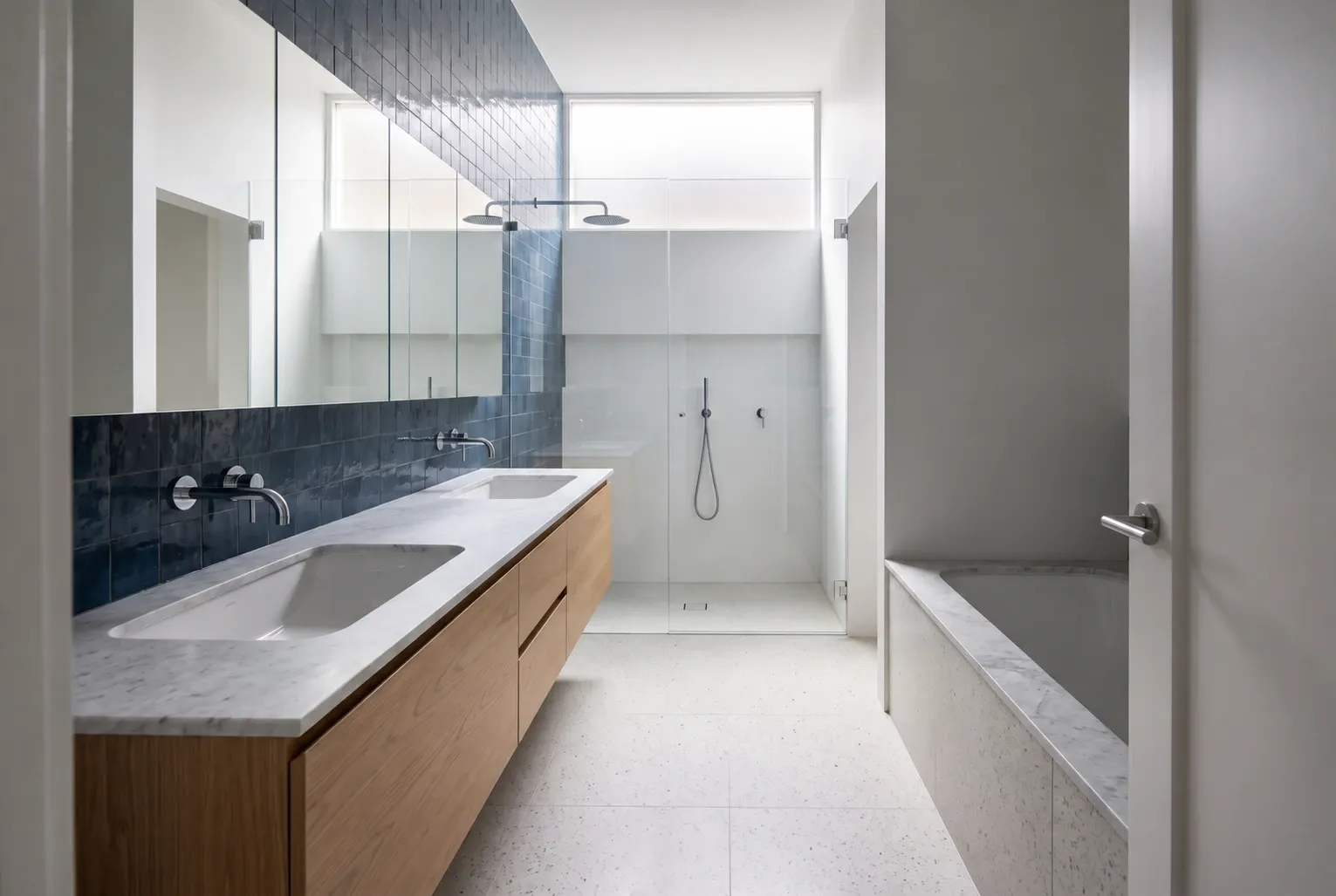 Inky blue tile and oak double vanity with matching pale marble vanity top and inset bath surround — bathroom design inspiration