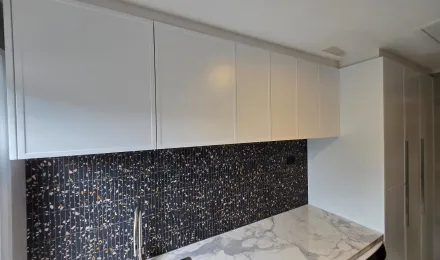 White overhead laundry cupboards above a mosaic splashback and stone benchtop