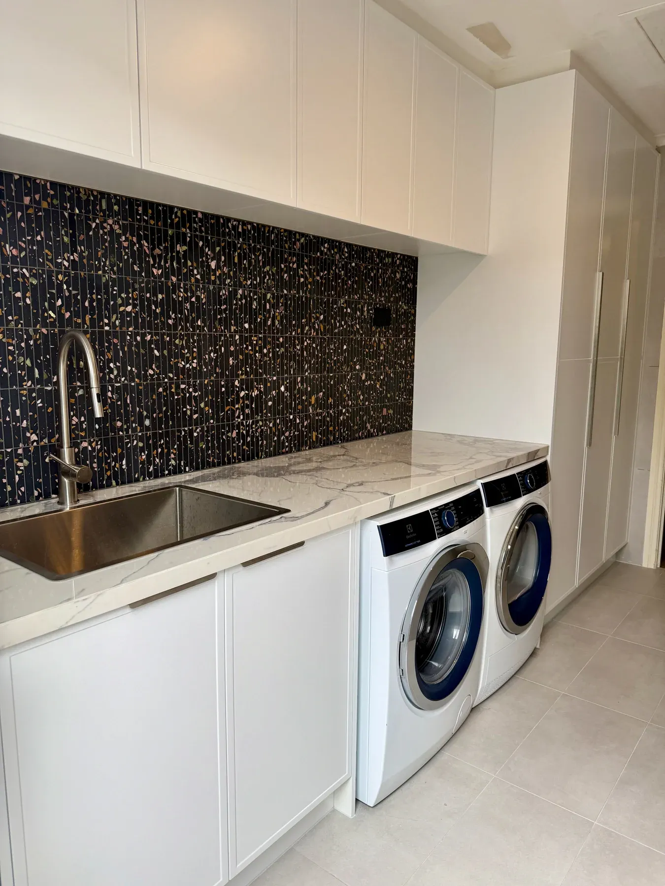 Completed laundry with mosaic splashback, white cabinetry, sink and under-bench washer and dryer