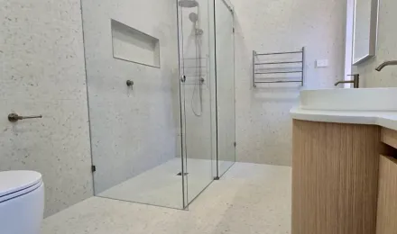 Glass shower with tiled niche beside the curved timber vanity in the completed bathroom