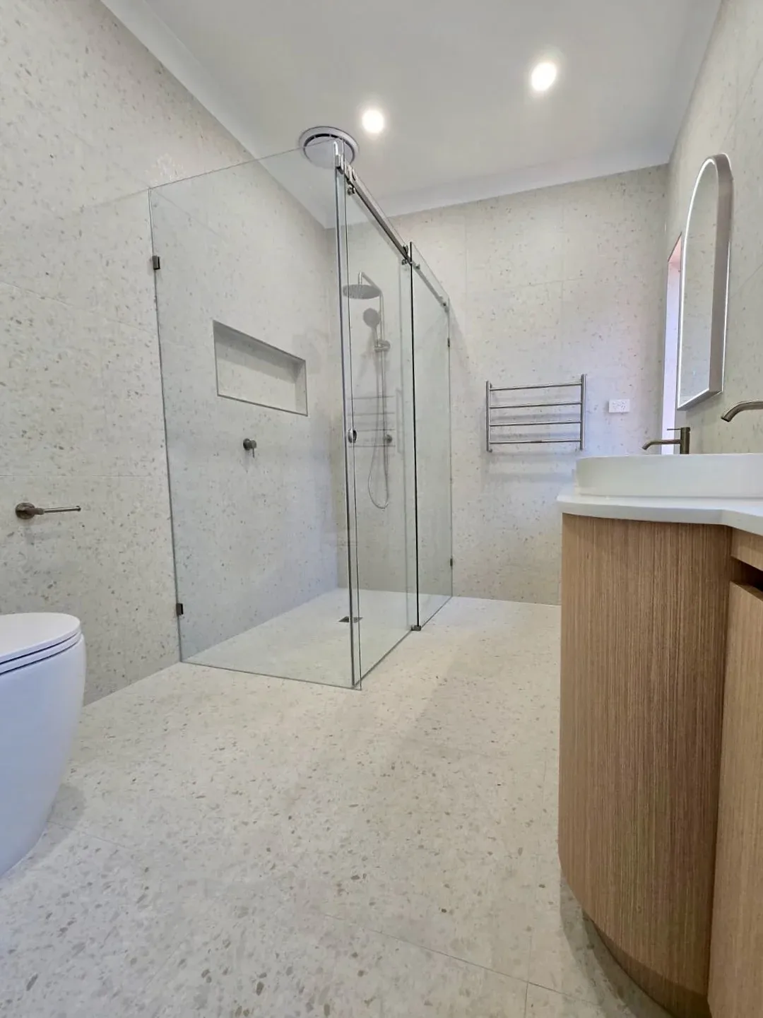 Glass shower with tiled niche beside the curved timber vanity in the completed bathroom