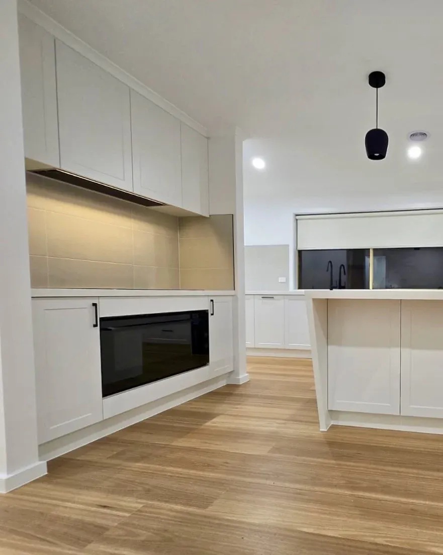 White kitchen cooking area with under-bench oven, overhead cabinetry and clear adjoining benchtop