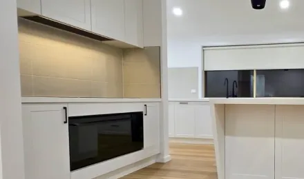 White kitchen cooking area with under-bench oven, overhead cabinetry and clear adjoining benchtop